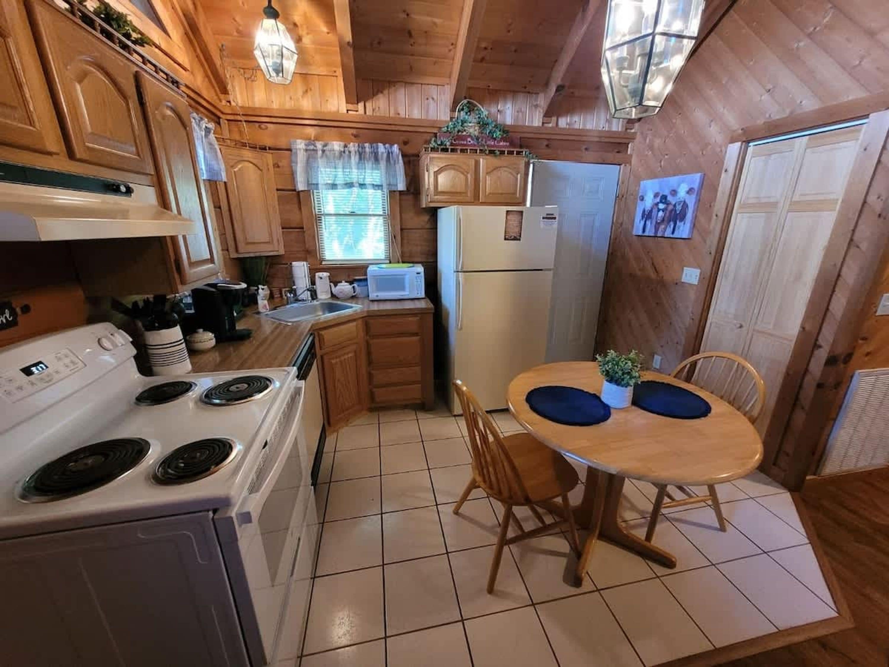 Une cuisine aménagée dans le style d’un chalet en bois, avec un fourneau, un four à micro-ondes, un réfrigérateur et une table à manger avec des chaises.