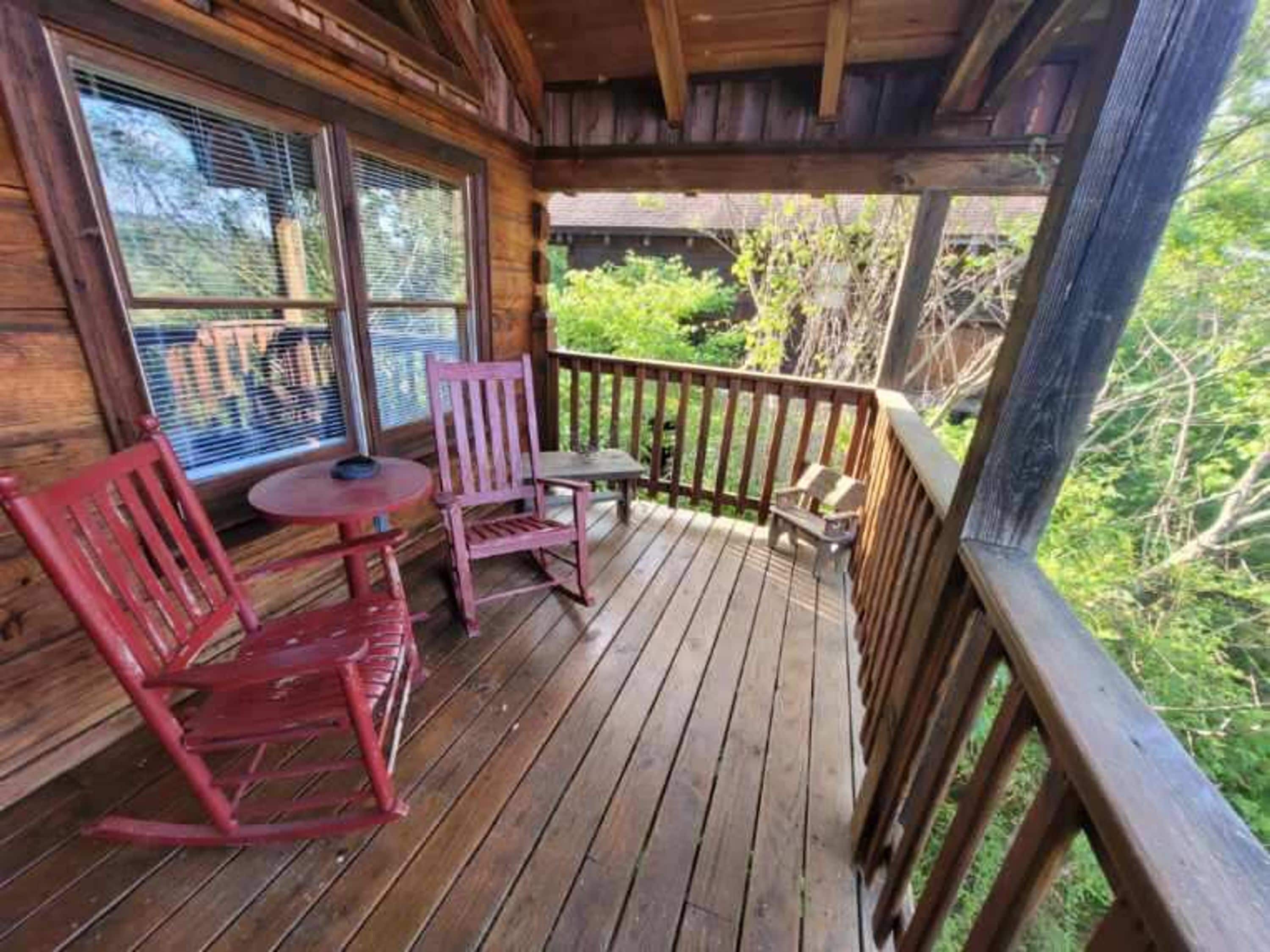 A wooden deck with a railing, two rocking chairs, and a small table.