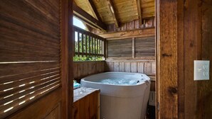 A wooden cabin with a hot tub, wooden walls, and a window with blinds.
