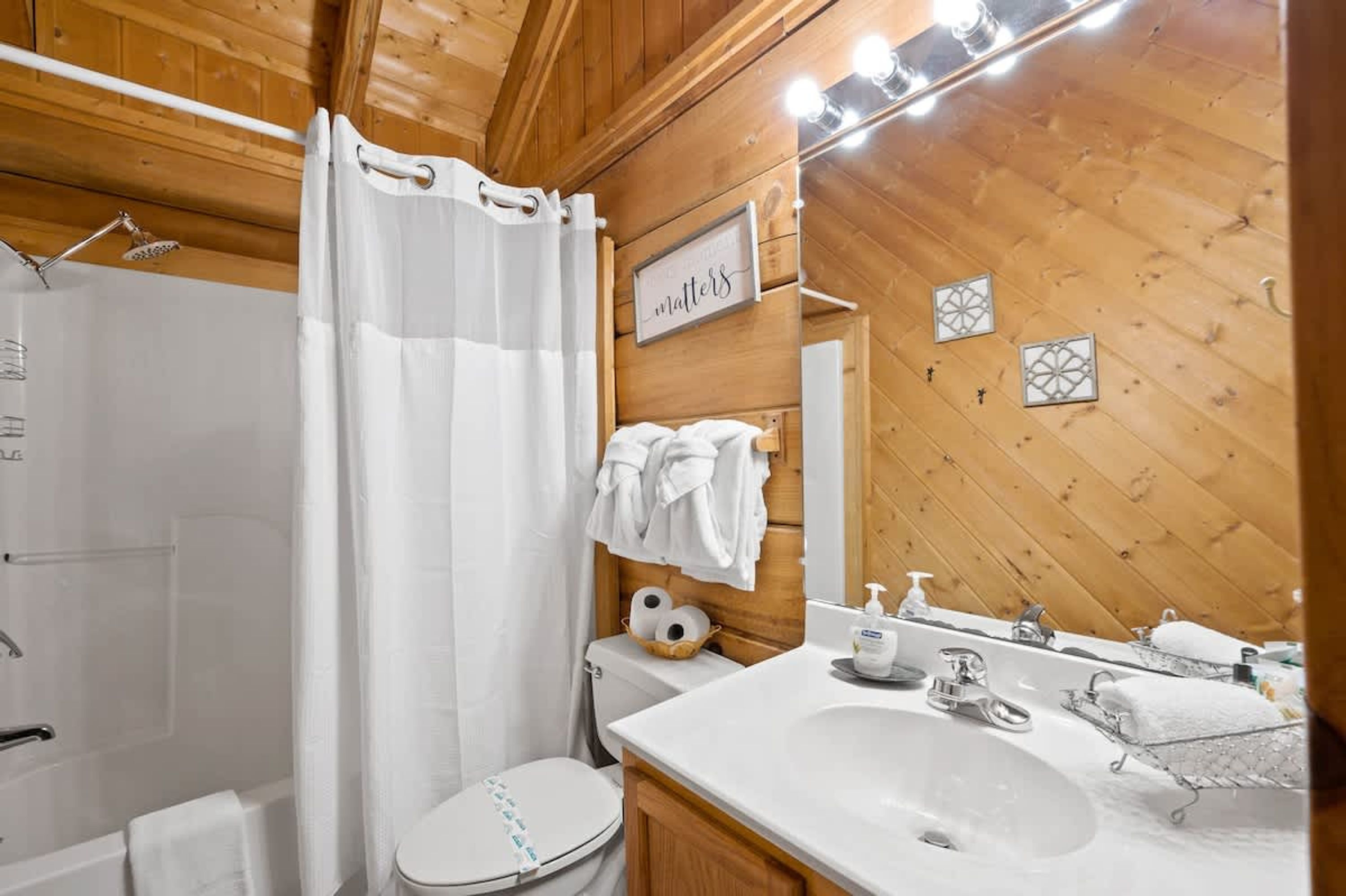 A bathroom with a wooden interior, a shower, a toilet, a sink with a mirror, and a towel rack.