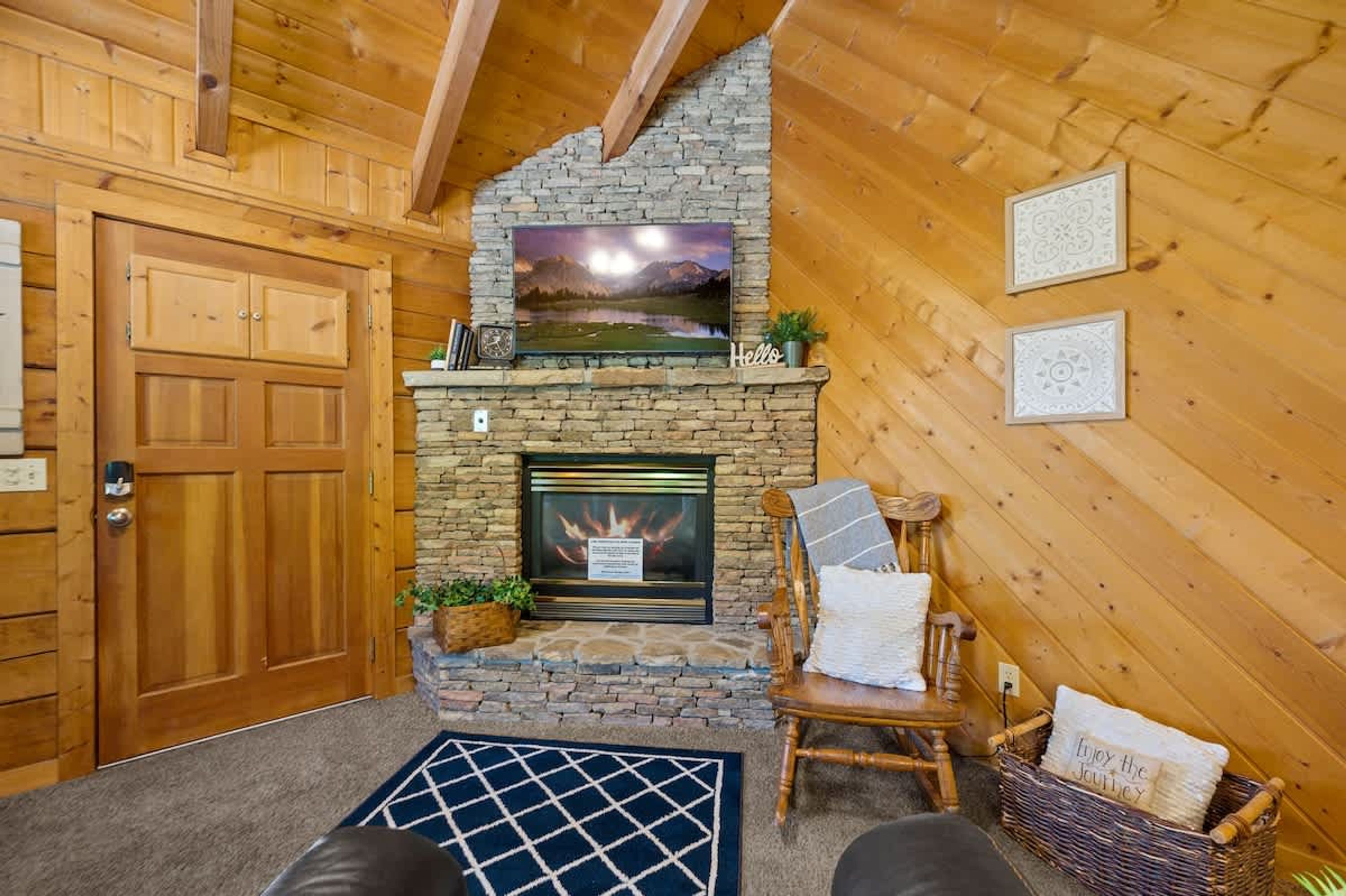 A cozy room with a stone fireplace, wooden walls, a door, a chair, and a rug.