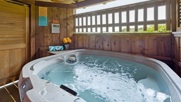 A wooden cabin with a hot tub, wooden walls, and a window with a view of greenery. - Location Smokies Log Cabin Hot Tub Fireplace (Pigeon Forge)