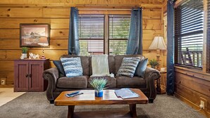 A cozy living room with a brown leather sofa, a wooden coffee table, and a framed picture on the wall. - Location Smokies Log Cabin Hot Tub Fireplace (Pigeon Forge)