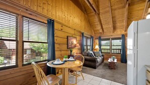 A cozy wooden cabin interior with a dining area, a sofa, and a refrigerator. - Location Smokies Log Cabin Hot Tub Fireplace (Pigeon Forge)