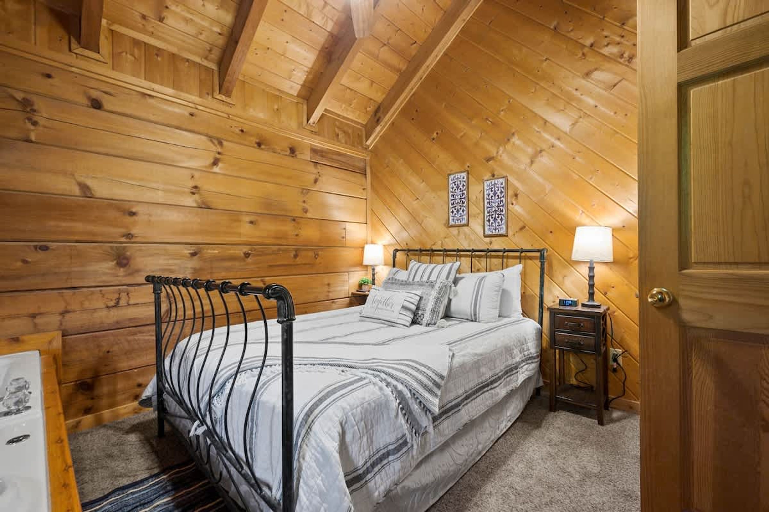 Een slaapkamer met houten lambrisering, een bed, bedlampen en een deur.