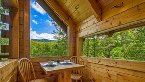 A wooden cabin with a dining area, large windows, and a view of a forested landscape. - Private Studio Log Cabin Hot Tub Fireplace Relax (Sevierville)