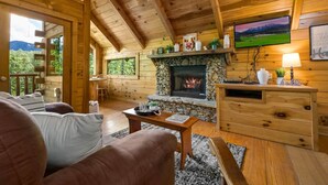 A cozy cabin interior with a stone fireplace, wooden furniture, and a television on the wall. - Private Studio Log Cabin Hot Tub Fireplace Relax (Sevierville)