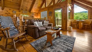 A cozy cabin interior with a brown leather sofa, wooden rocking chair, and a dining table with chairs. - Private Studio Log Cabin Hot Tub Fireplace Relax (Sevierville)