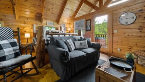 A cozy cabin interior with a wooden ceiling, a sofa, a rocking chair, a dining table, and a clock on the wall. - Private Studio Log Cabin Hot Tub Fireplace Chill (Sevierville)