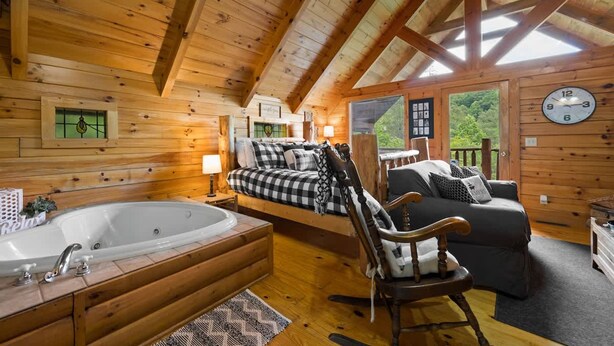 A log cabin interior with a large wooden ceiling, a cozy bed, a sofa, a rocking chair, and a bathtub. - Private Studio Log Cabin Hot Tub Fireplace Chill (Sevierville)