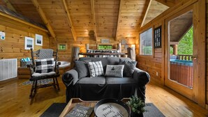 A cozy cabin interior with a wooden ceiling, a black sofa with patterned cushions, a wooden rocking chair, and a dining table. - Private Studio Log Cabin Hot Tub Fireplace Chill (Sevierville)