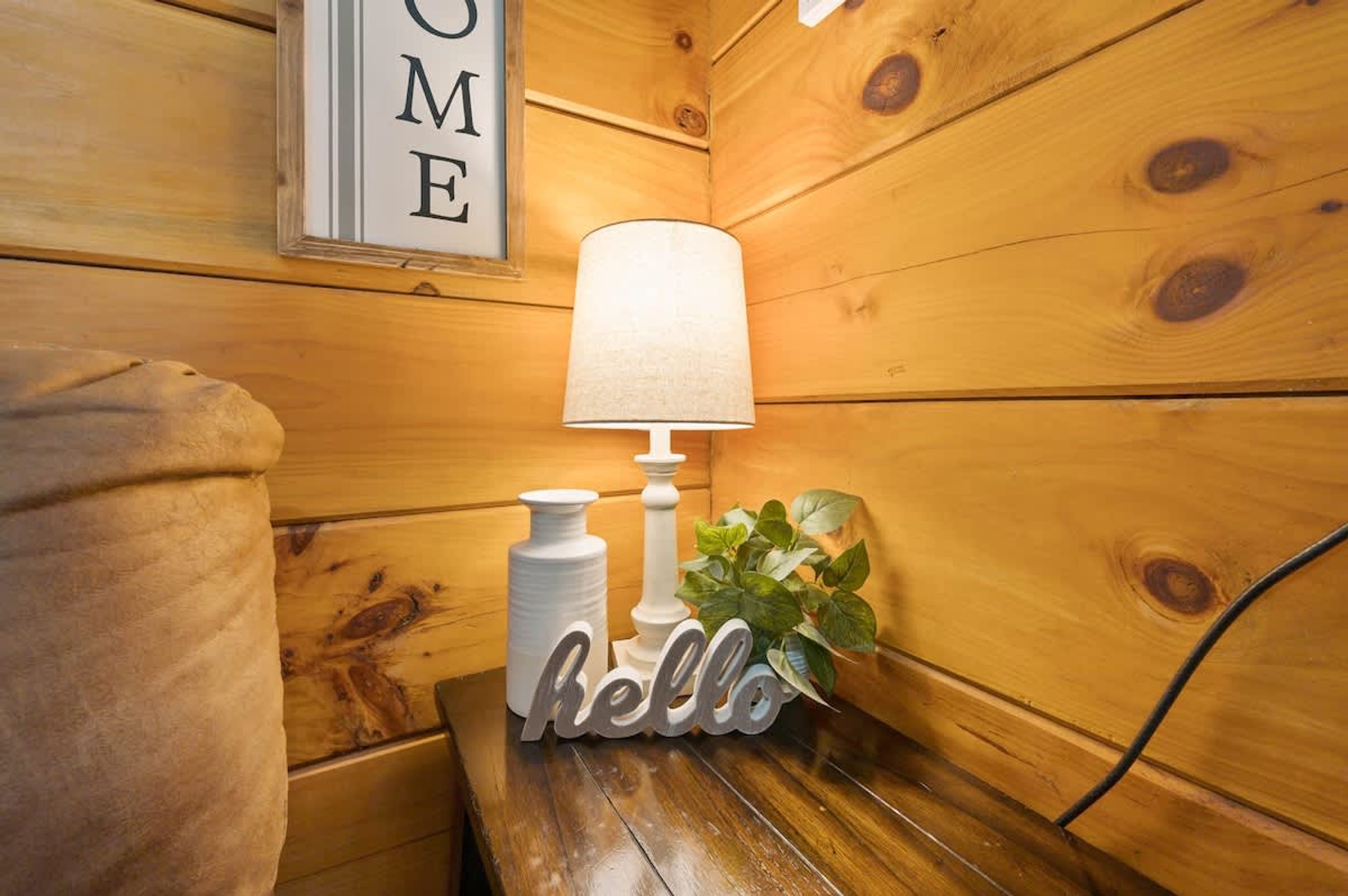 En stuga med träpanel på insidan, med en mysig hörna som innehåller en lampa, en skylt med texten ”hej” och en inramad skylt med texten ”HEM” på väggen.