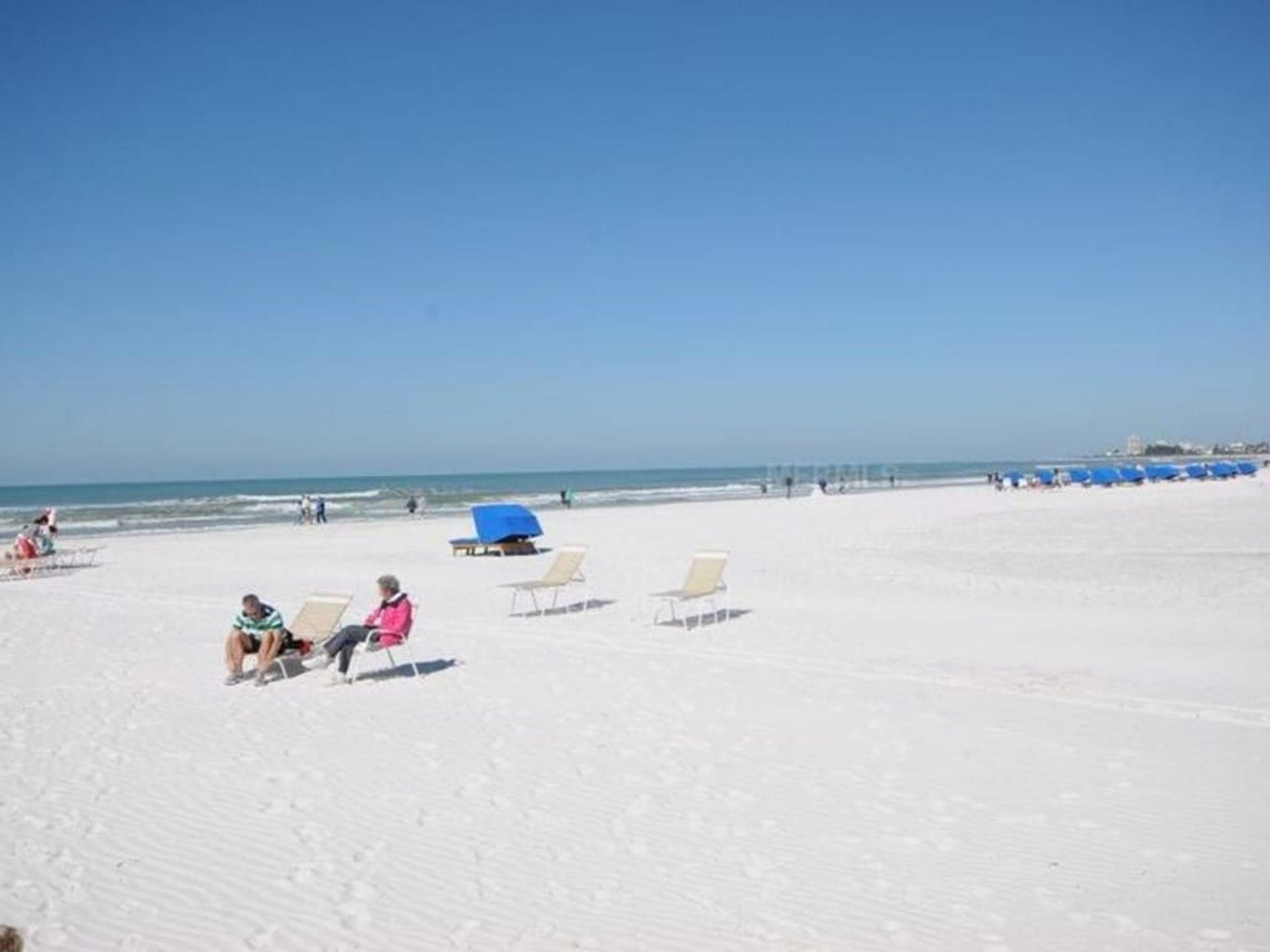 A beach with white sand, a few people, and blue umbrellas.