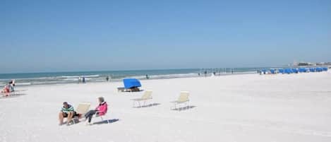 A beach with white sand, a few people, and blue umbrellas.