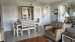 Un comedor con una mesa y sillas blancas, una araña y un sofá color beige en una sala de estar.