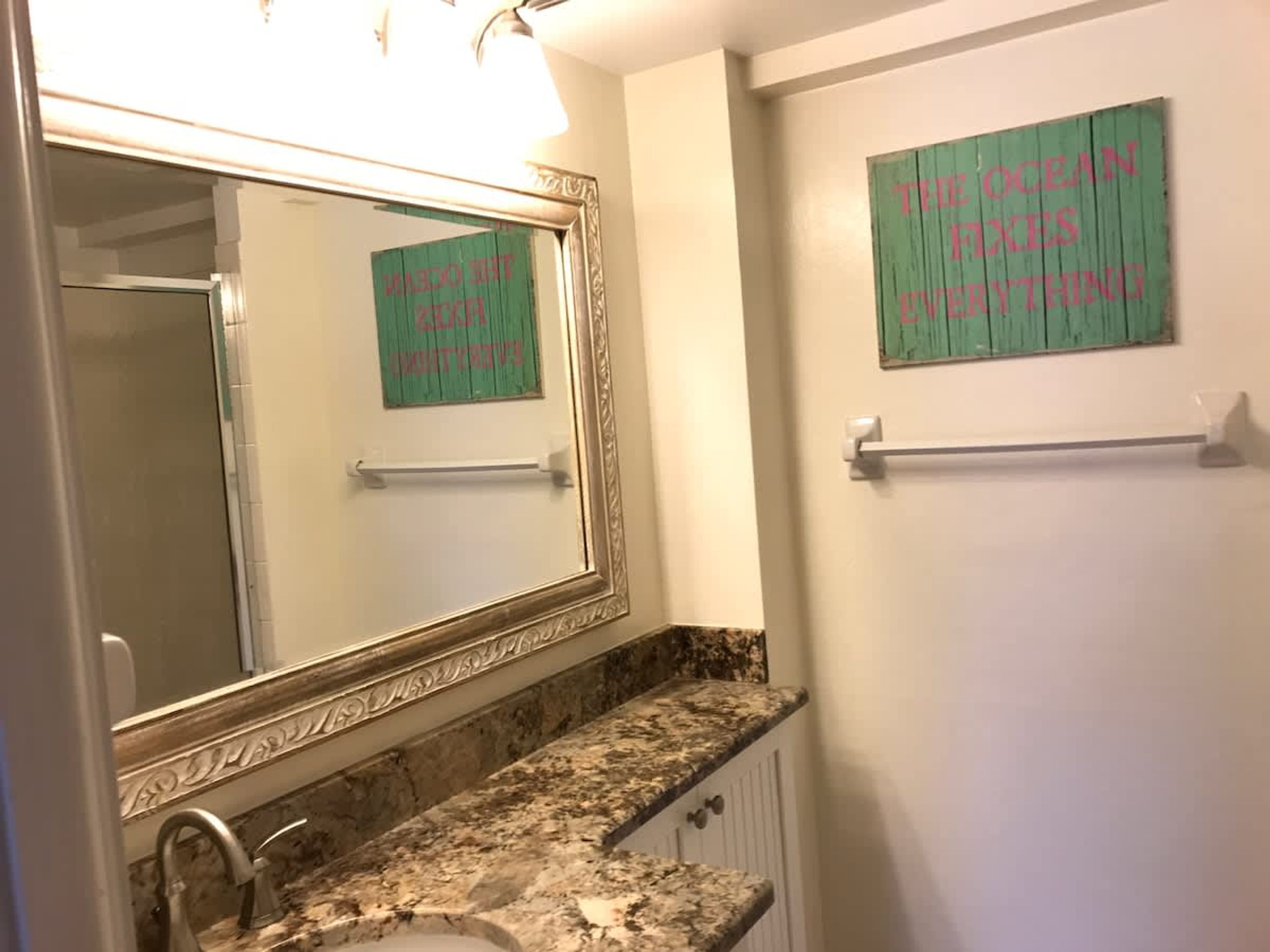 A bathroom with a marble countertop, a large mirror, and a towel rack.