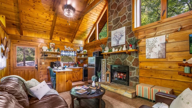 Ein gemütliches Blockhaus-Interieur mit Kamin aus Stein, Holzwänden, einer Ledersofa und einer Küchenzeile.