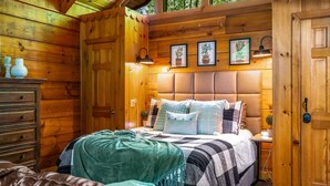 Ein schlicht eingerichtetes Schlafzimmer im Blockhausstil mit einem großen Bett, einem Schminktisch und einem Nachttisch.