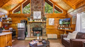 Ein gemütliches Blockhaus mit Kamin aus Naturstein, Holzwänden, einer Küchenzeile und einer komfortablen Sitzecke mit Ledersofa und Couchtisch.
