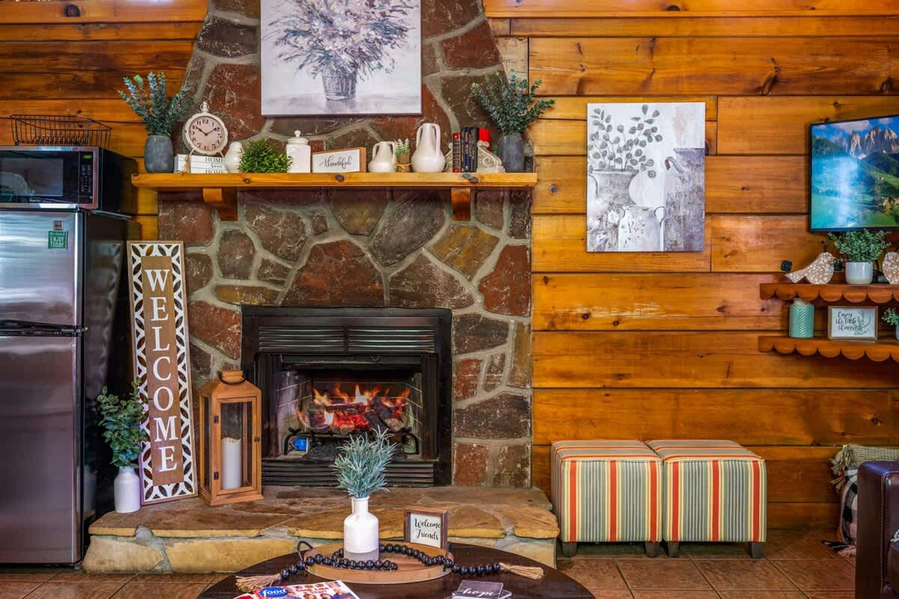 A cozy cabin interior with a stone fireplace, wooden walls, a welcome sign, and a television mounted on the wall.