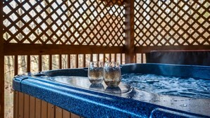 A hot tub with two glasses on the edge, surrounded by a wooden lattice structure. - Location-quiet-hottub-fireplace (Sevierville)