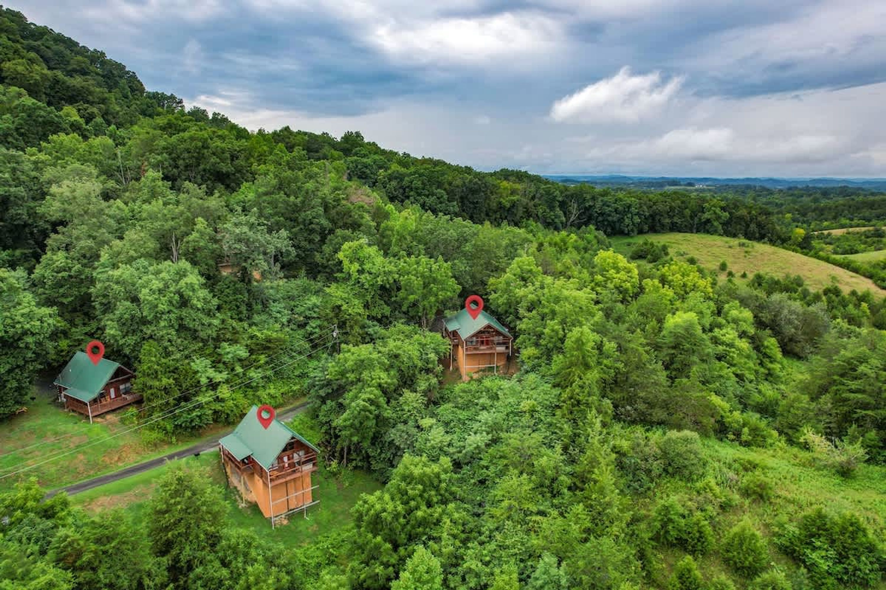 Three wooden cabins surrounded by dense forest, with a road leading to them.