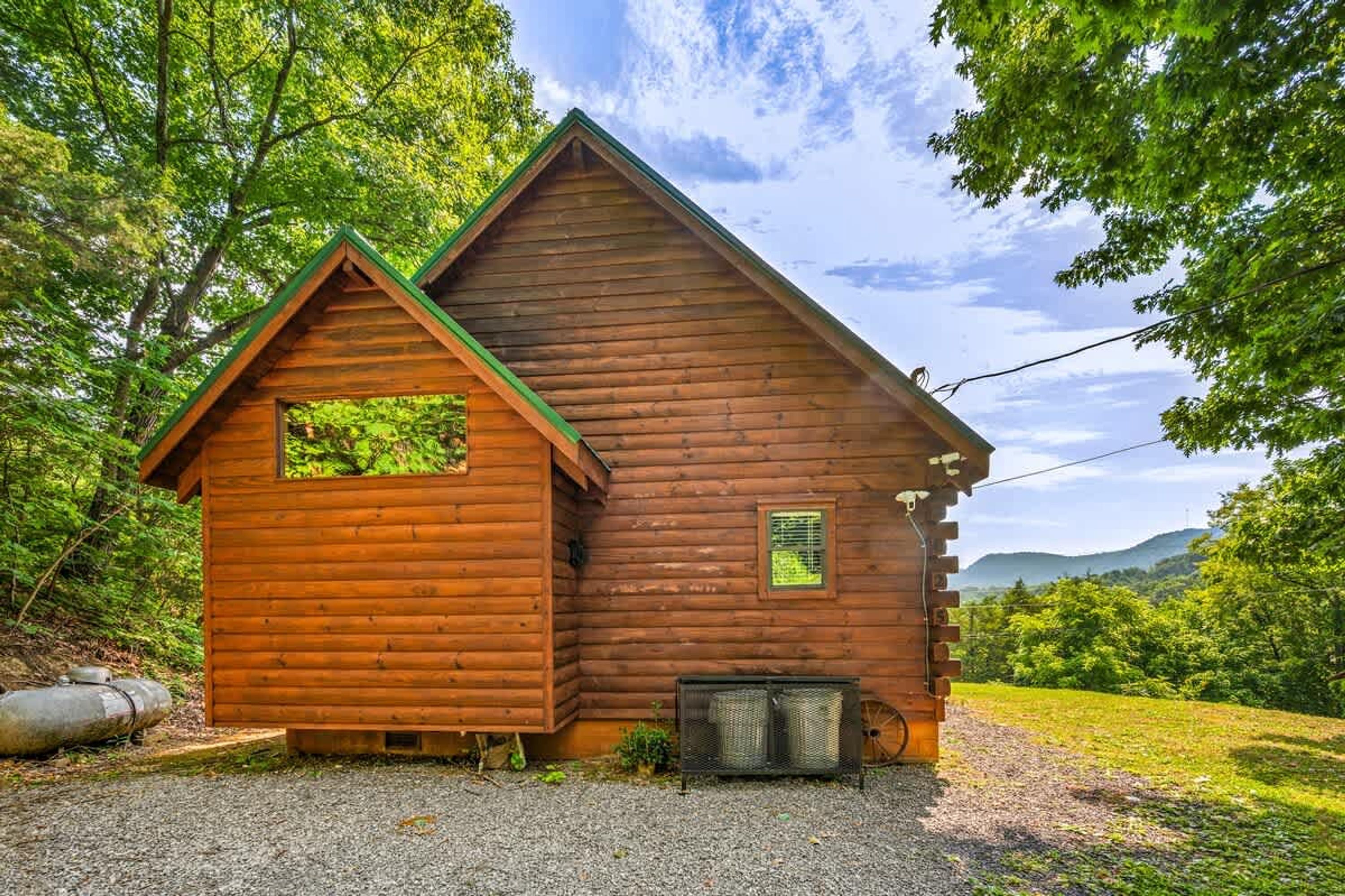 A wooden cabin with a green roof, a small porch, and a gravel driveway.