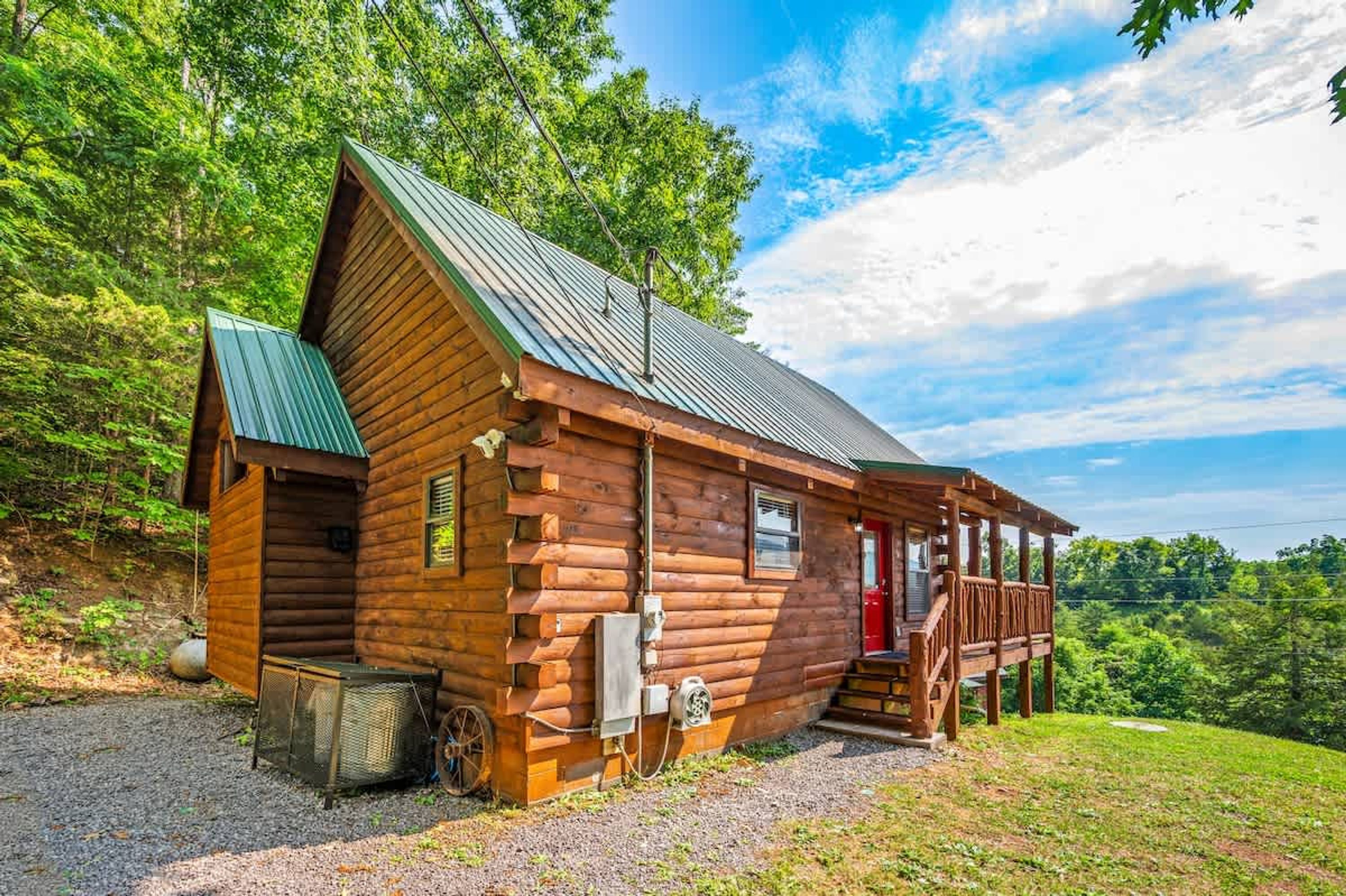 A wooden cabin with a metal roof, a porch, and a gravel driveway.