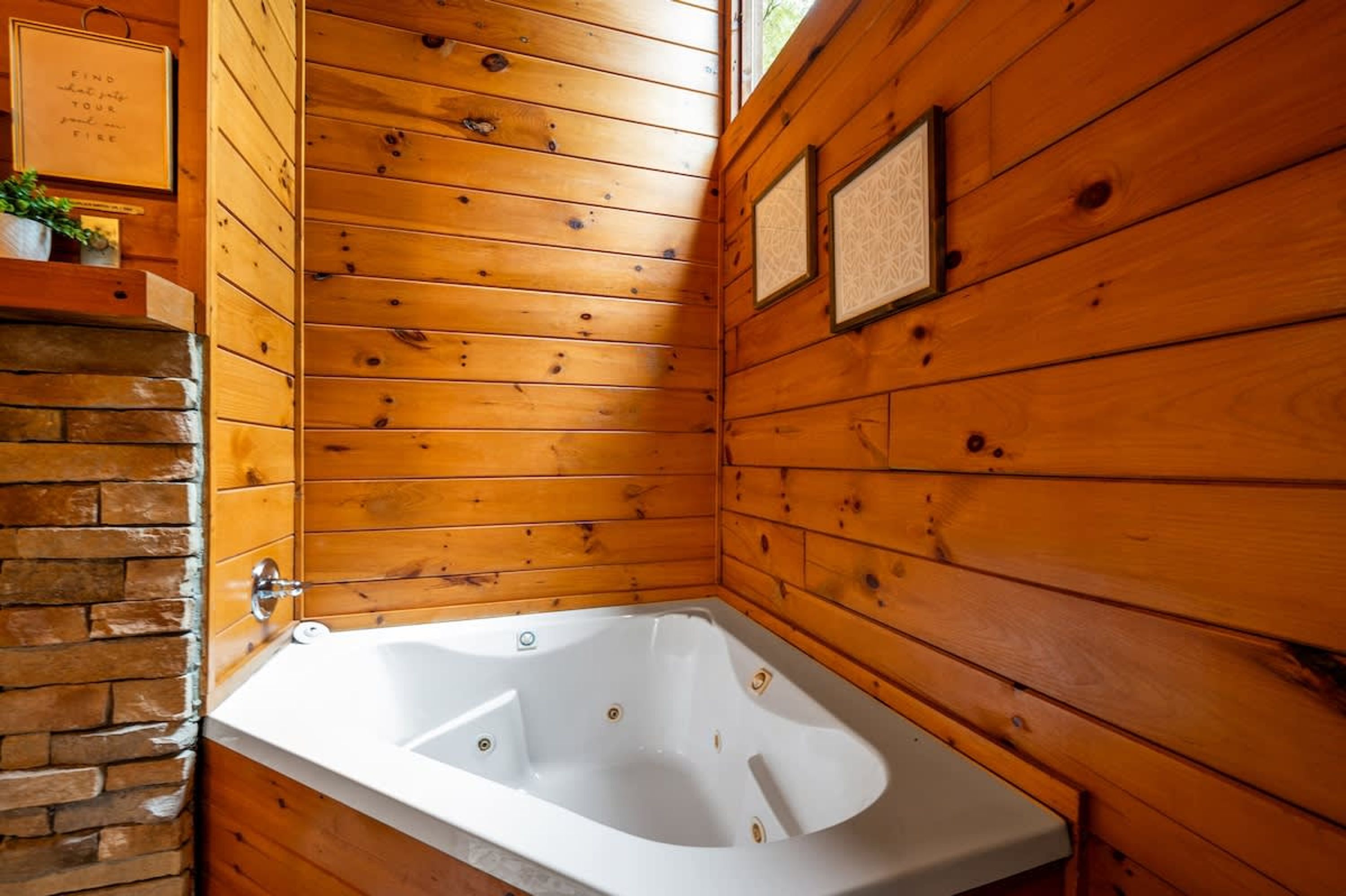 Una cabaña de madera con una bañera blanca, paredes de madera y una chimenea de ladrillo.