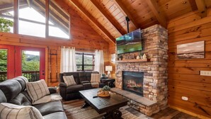 A cozy cabin interior with a stone fireplace, wooden walls, and a leather sofa. - View-location-hot Tub-pool Table-3 Fireplaces (Sevierville)
