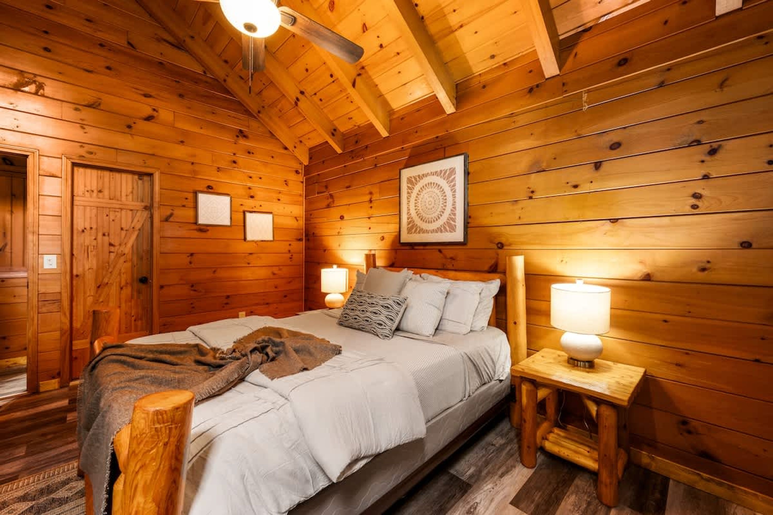 Ein gemütliches Schlafzimmer in einer Holzhütte mit einem Bett, zwei Nachttischlampen und einem gerahmten Kunstwerk an der Wand.