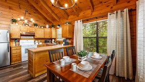 A wooden cabin-style kitchen with wooden cabinets, a central island, and a dining area with a table set for four. - View-location-hot Tub-pool Table-3 Fireplaces (Sevierville)