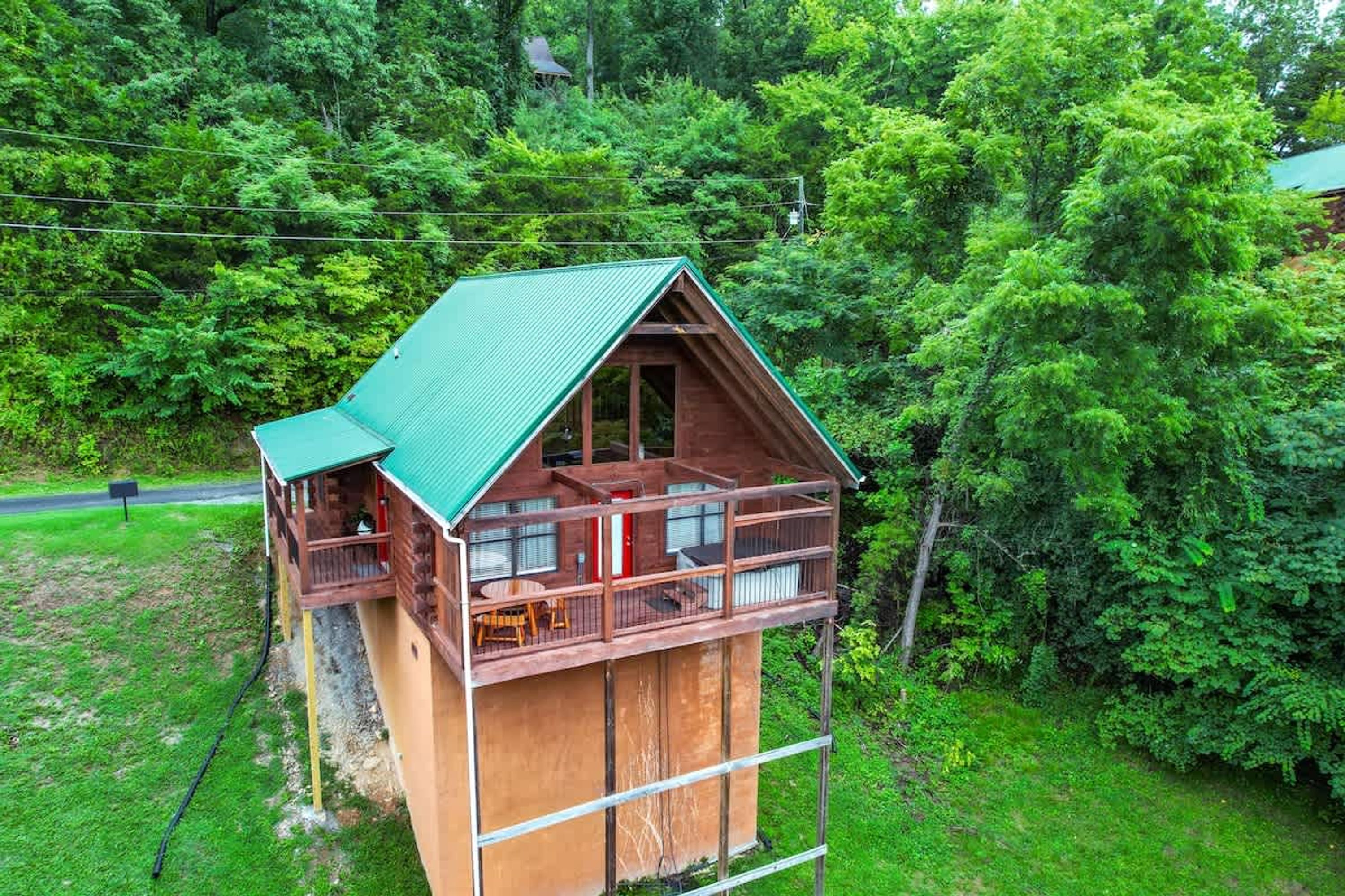Une cabane en bois avec un toit vert, un balcon et un petit espace extérieur aménagé pour s’asseoir.