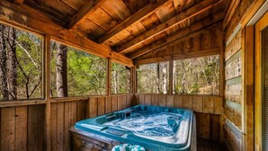 Una cabaña de madera con jacuzzi, ventanas amplias y vistas al bosque.