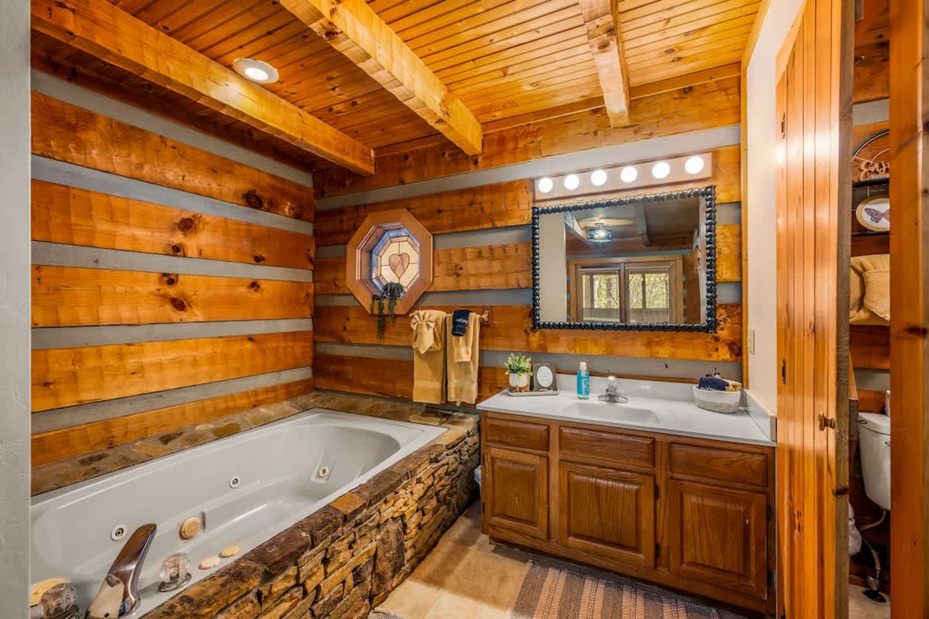 Une salle de bain avec un mur en pierre, un lambris en bois, une grande baignoire, un lavabo avec un miroir et un porte-serviettes.