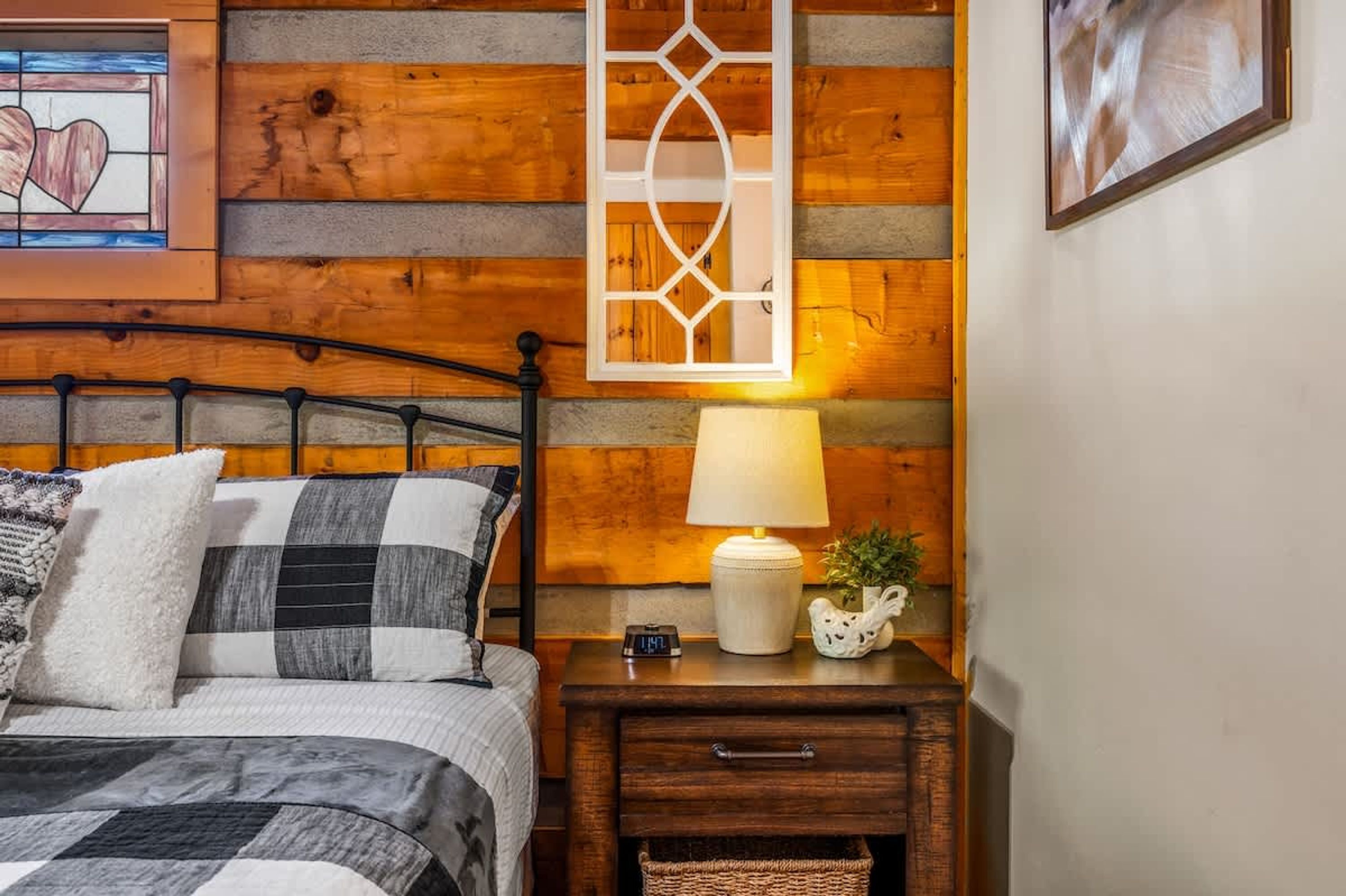 Un dormitorio con pared de troncos de madera, una cama con manta a cuadros, una mesita de noche con lámpara y un adorno en la pared.