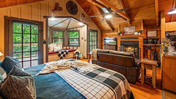 A cozy log cabin interior with a large bed, a fireplace, a leather sofa, and a dining area. - Secluded Cabin in the Woods-hot Tub-quiet-fireplace-honeymoon (Sevierville)