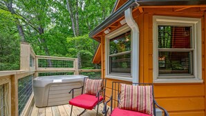 A wooden deck with a hot tub, two rocking chairs with red cushions, and a window with blinds. - Secluded Cabin in the Woods-hot Tub-quiet-fireplace-honeymoon (Sevierville)