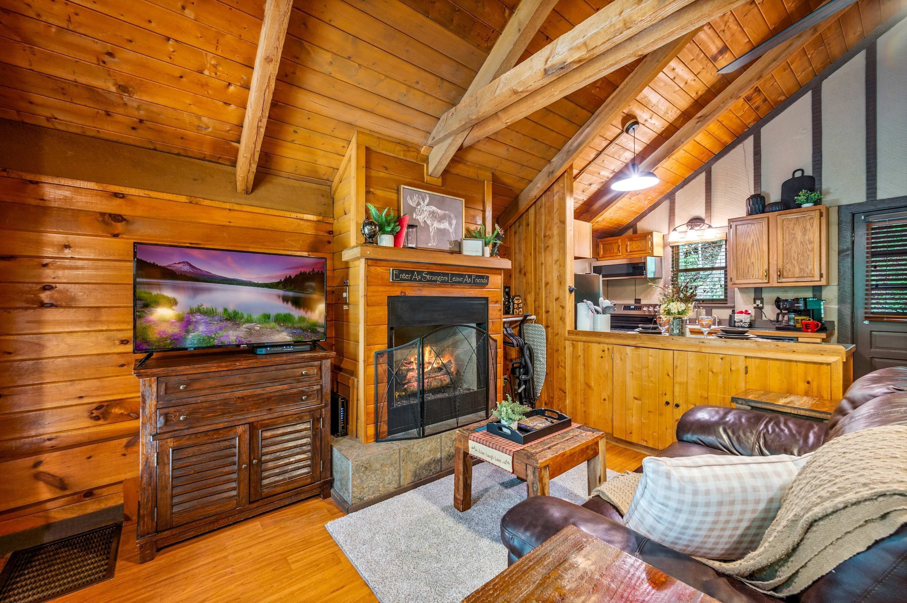A cozy cabin interior with a fireplace, wooden walls, a television, and a leather couch.