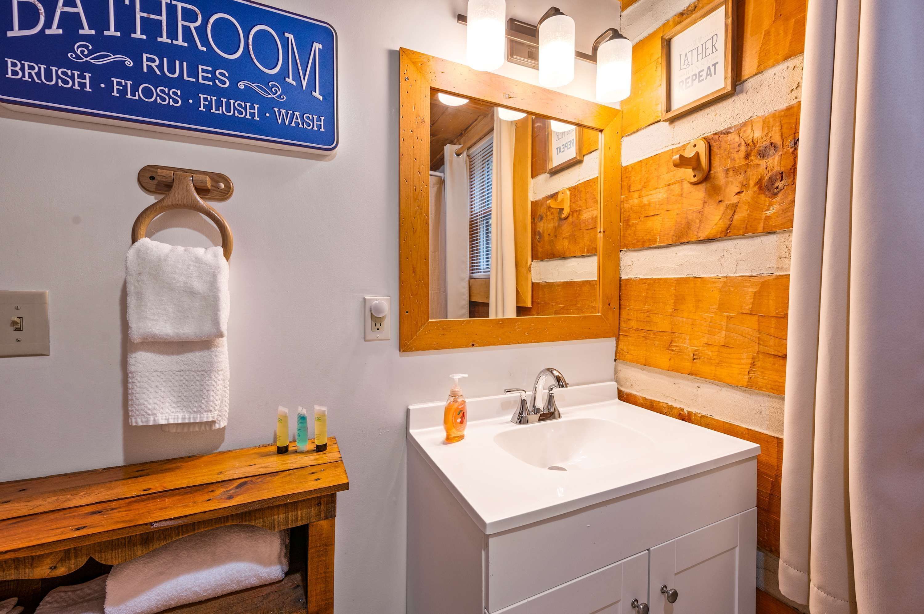 A bathroom with a wooden vanity, a white sink, and a mirror. There is a sign above the sink that lists bathroom rules.