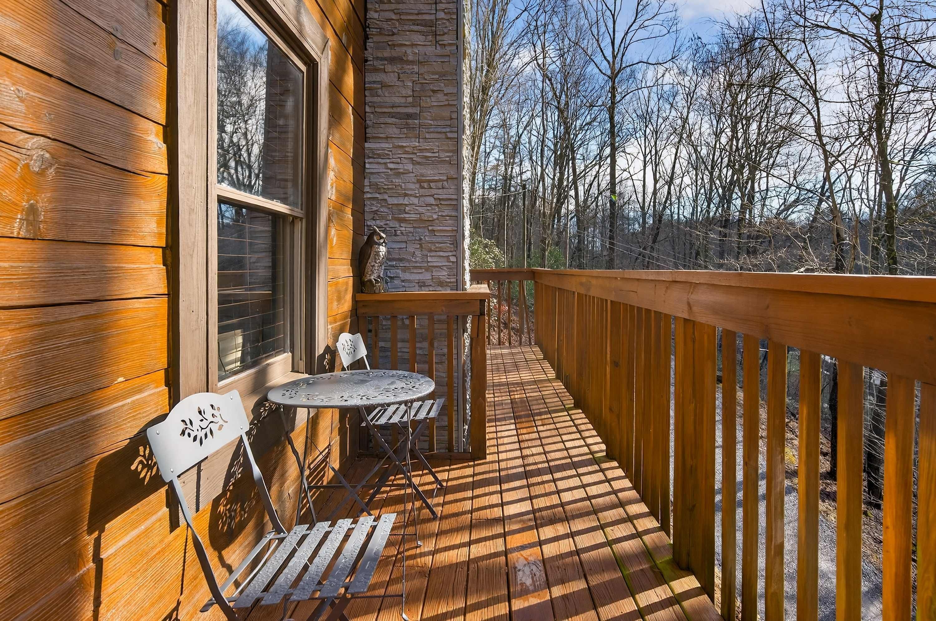 A wooden deck with a table and chairs, a stone wall, and a view of trees.