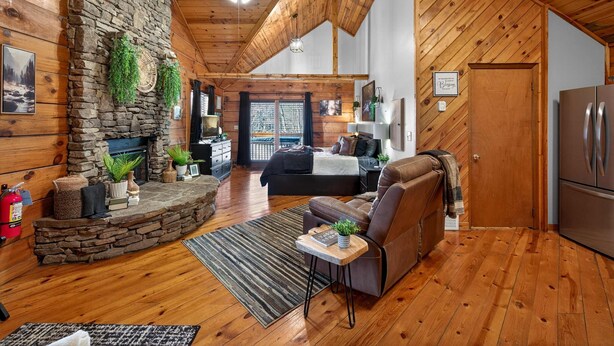 L’intérieur d’un chalet accueillant, avec une cheminée en pierre, des murs en bois, un canapé et un coin cuisine.