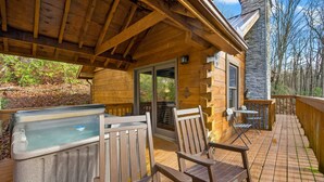 Une terrasse en bois avec un jacuzzi, des chaises et un mur en pierre.