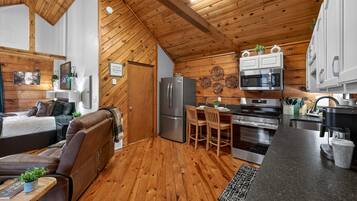 A compact living space with a kitchenette, wooden ceiling, and a cozy seating area.
