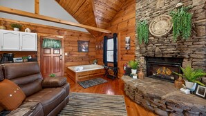 Un intérieur de chalet chaleureux avec une cheminée en pierre, des murs en bois, un canapé en cuir et une petite salle de bain.