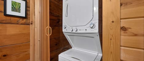 A white washer and dryer in a wooden cabin with a framed picture on the wall.