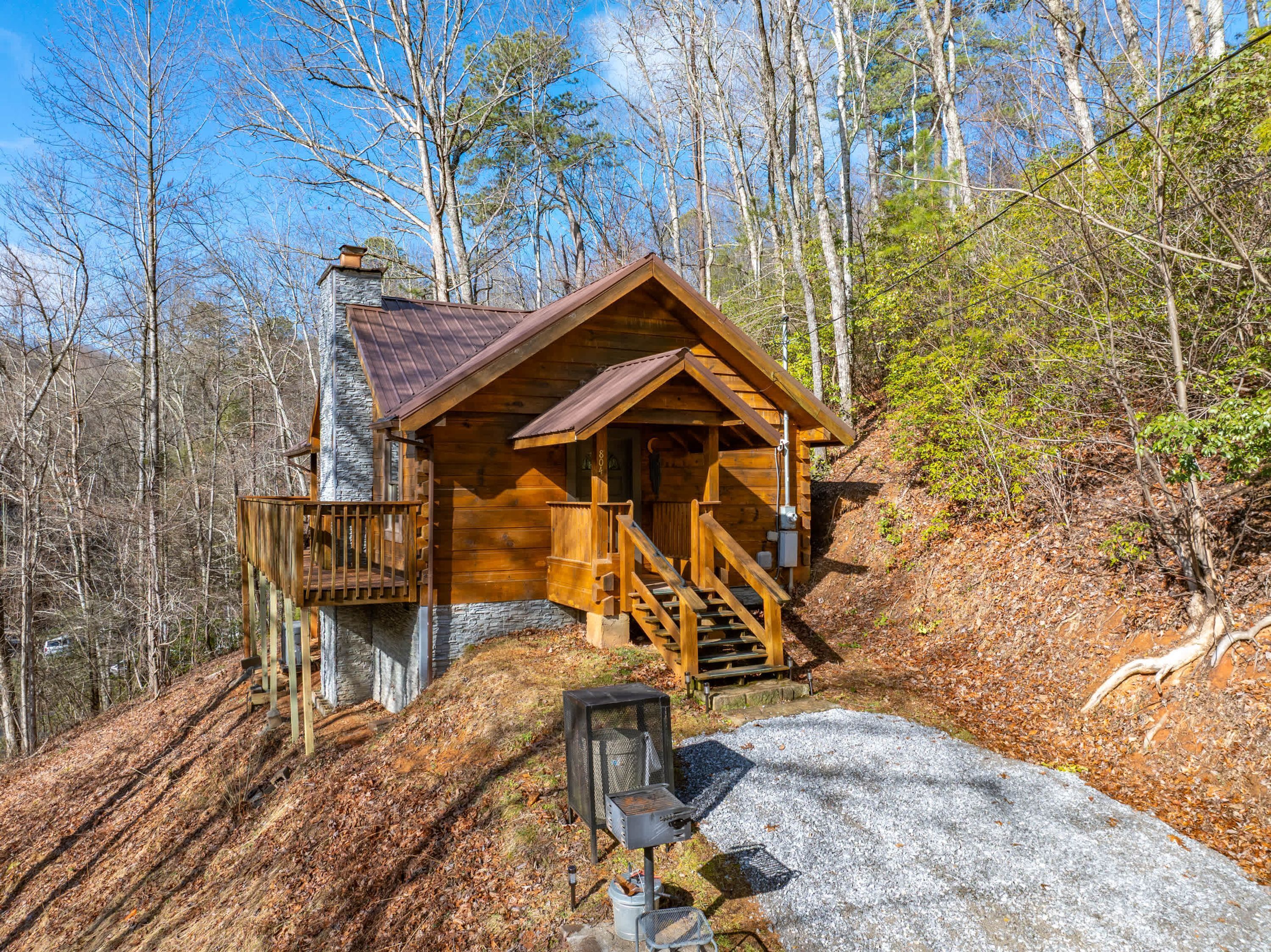A wooden cabin with a stone chimney, wooden deck, and a staircase leading to the entrance.