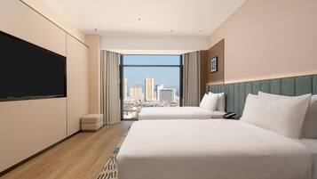 A hotel room with a large bed, a flat-screen TV, a city view, and a small seating area.