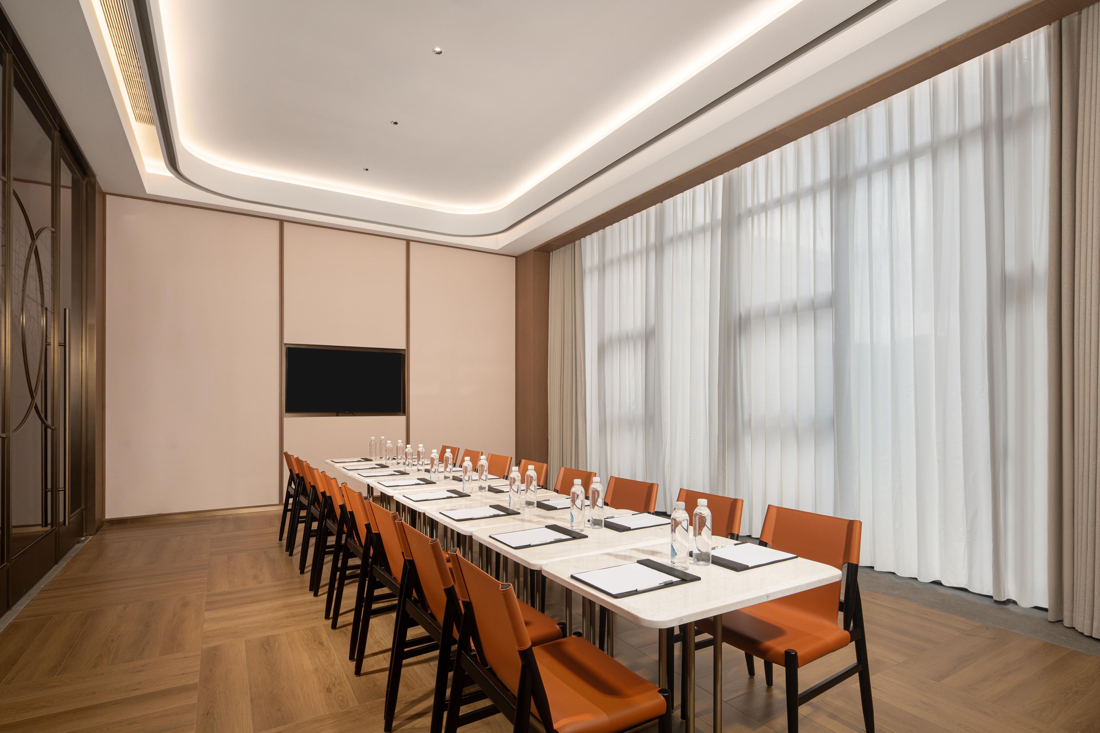 A conference room with a long table, chairs, a projector screen, and a large window with curtains.