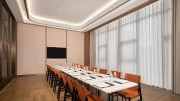 A conference room with a long table, chairs, a projector screen, and a large window with curtains.